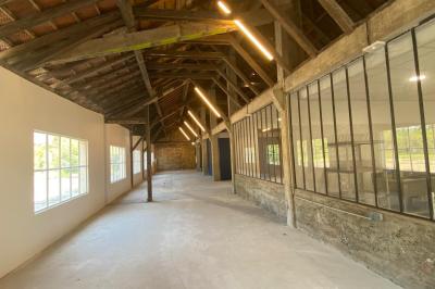 Miniature Location salle Toulouse-le-Château (Jura) - Forges de Baudin #4 Intérieur d'une grande pièce en pierre avec plafond en poutres apparentes, sol en dalles et lumière naturelle.