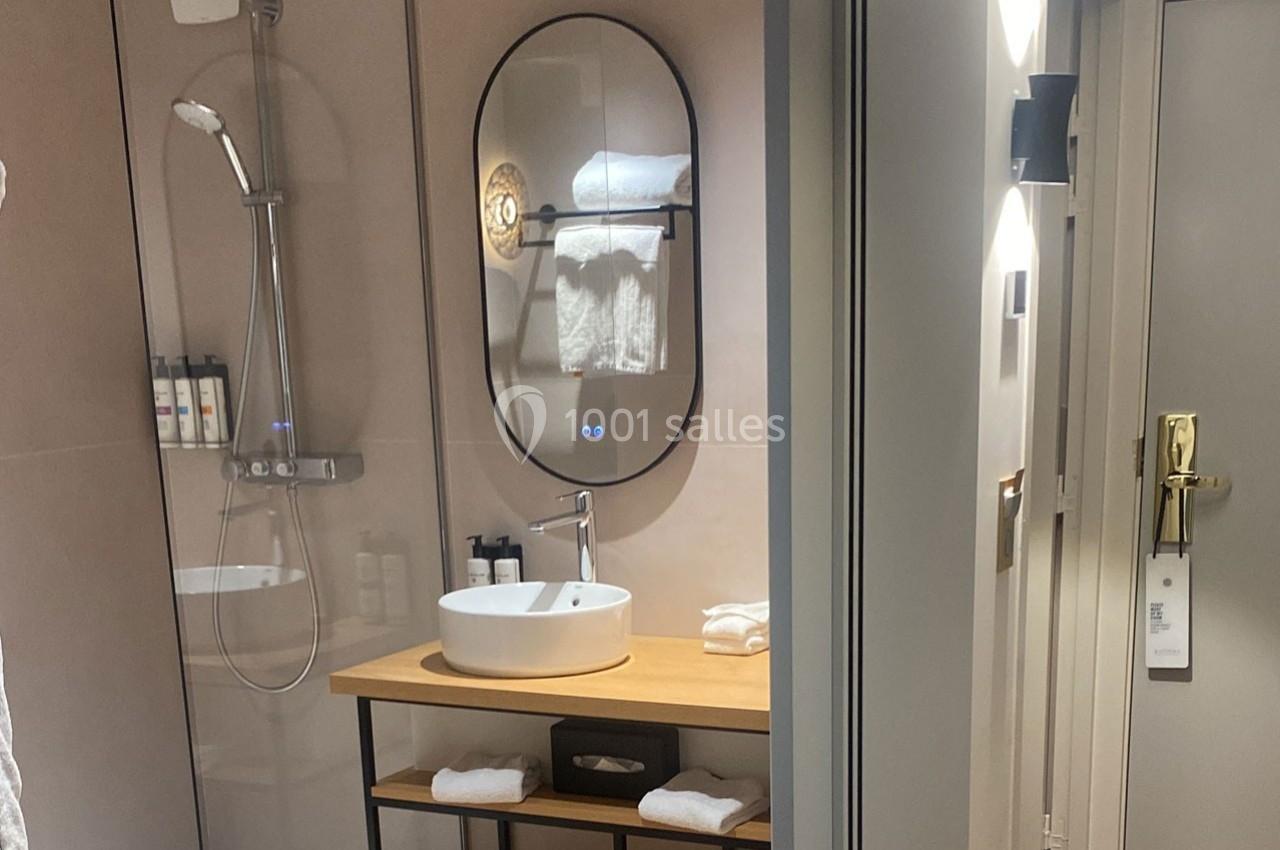 Salle de bain moderne avec douche à l'italienne, miroir ovale, lavabo sur meuble en bois et serviettes pliées.