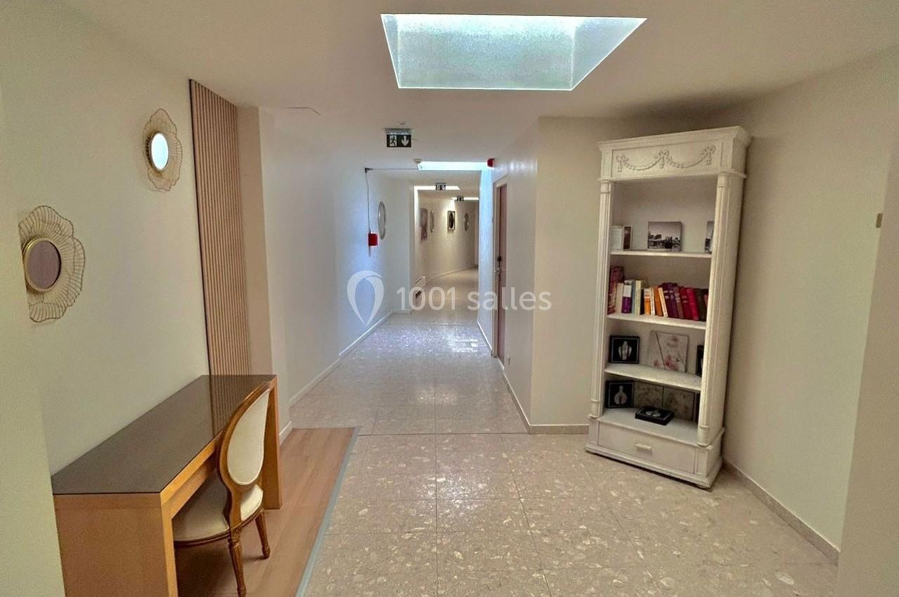 Couloir intérieur lumineux avec un bureau, une chaise et une étagère garnie de livres et décorations.