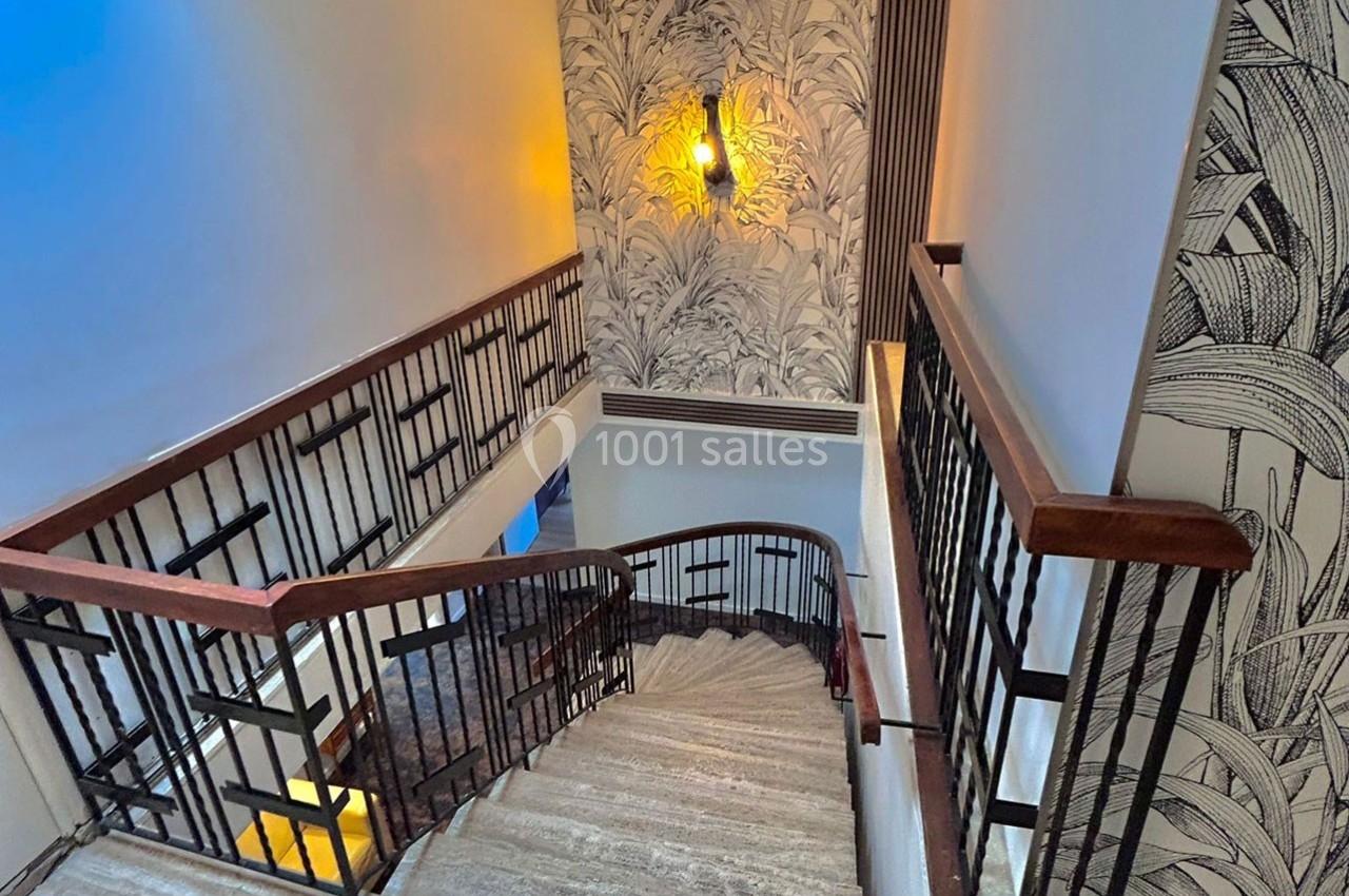 Escalier intérieur en bois et métal avec murs décorés de motifs végétaux et éclairage mural chaleureux.