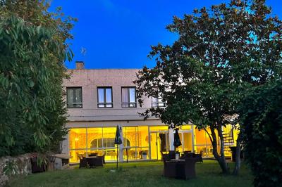 Petit jardin avec une table et des chaises roses, entouré de plantes et d'un puits en pierre devant des maisons.