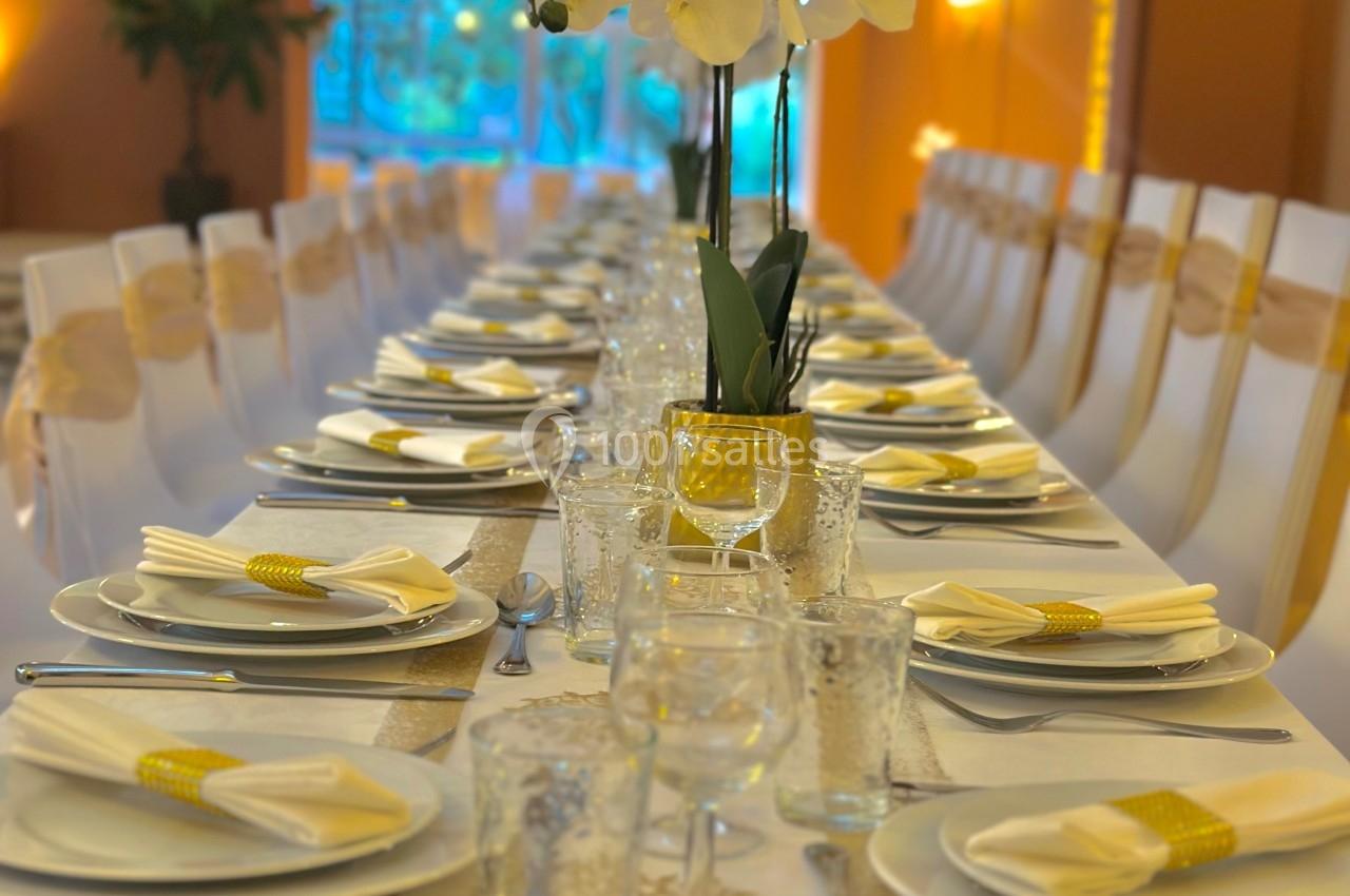 Table élégamment dressée avec nappes blanches, orchidée centrale, vaisselle et serviettes soigneusement disposées.