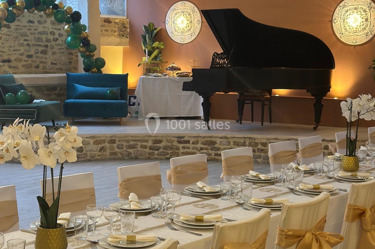 Salle de réception décorée avec des tables dressées, un piano à queue, des ballons et des orchidées blanches.