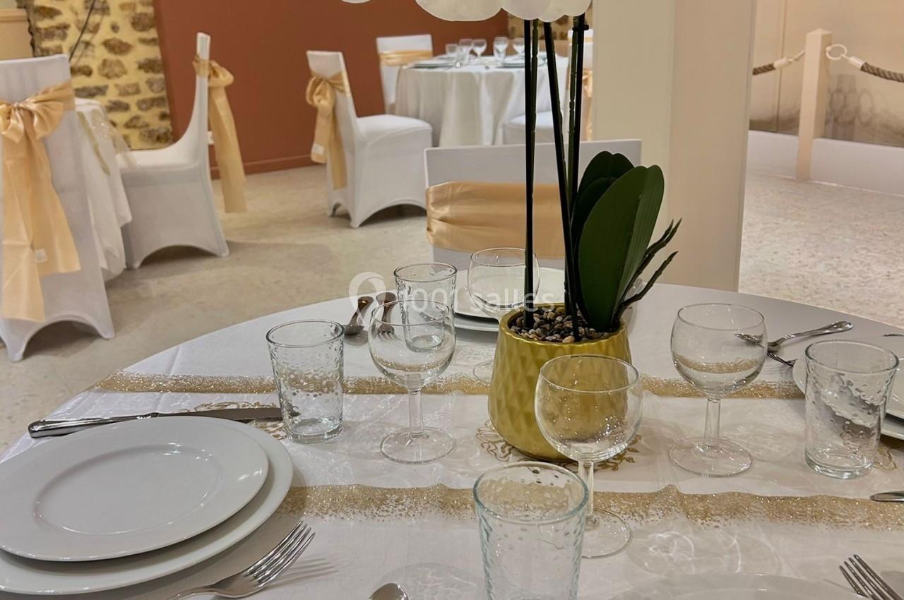 Table dressée avec vaisselle blanche, couverts argentés, nappe blanche et centre de table avec orchidées blanches.