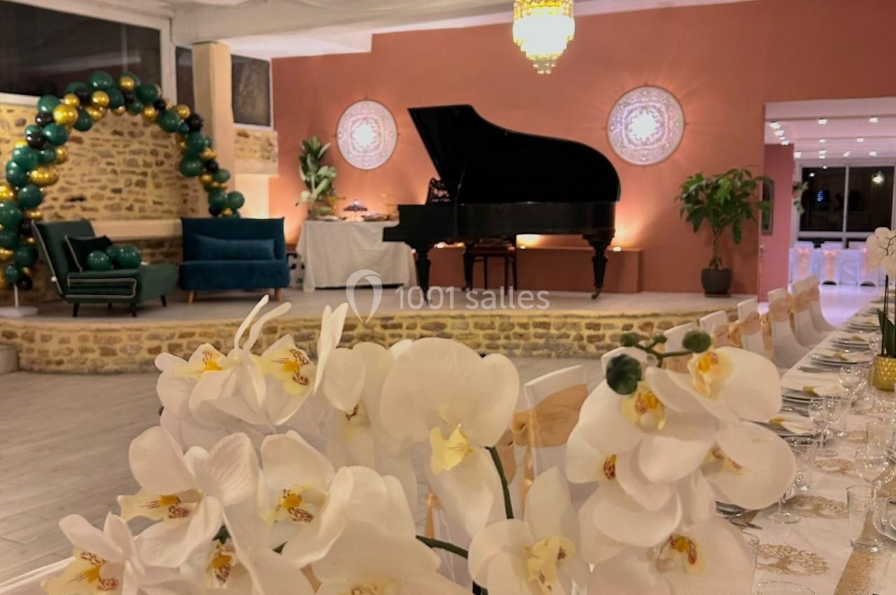 Salle décorée pour un événement avec table dressée, orchidées blanches au premier plan et piano à queue en arrière-plan.