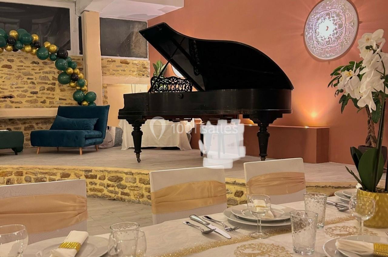 Salle élégante avec piano à queue noir, table dressée avec vaisselle raffinée et décoration florale, éclairage chaleureux.