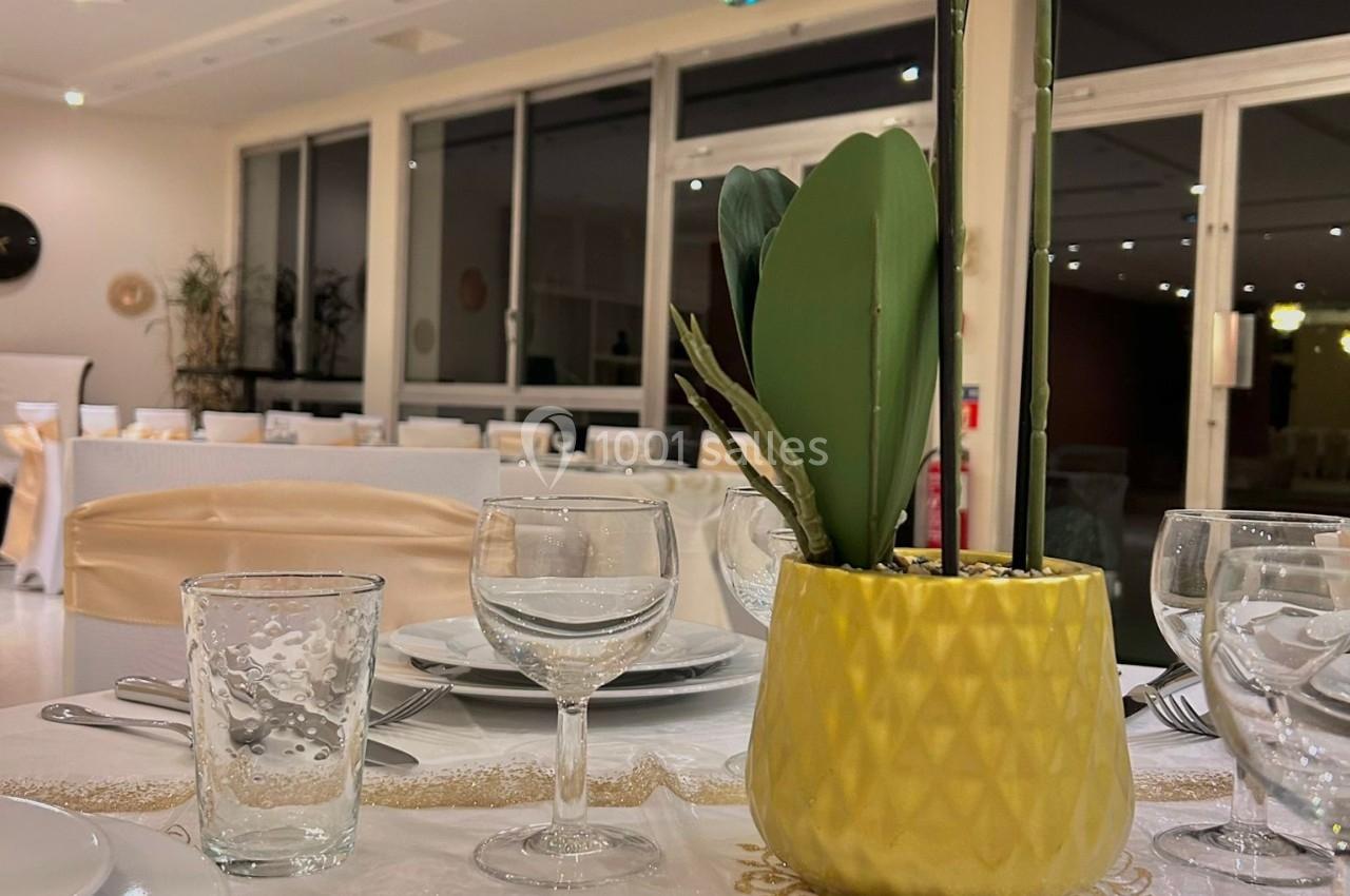 Table élégamment dressée avec vaisselle blanche, verres et une orchidée blanche dans un pot doré au centre.