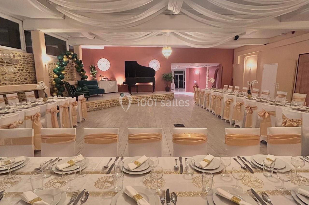 Salle de réception décorée avec des tables dressées, un piano à queue sur une estrade et un éclairage chaleureux.