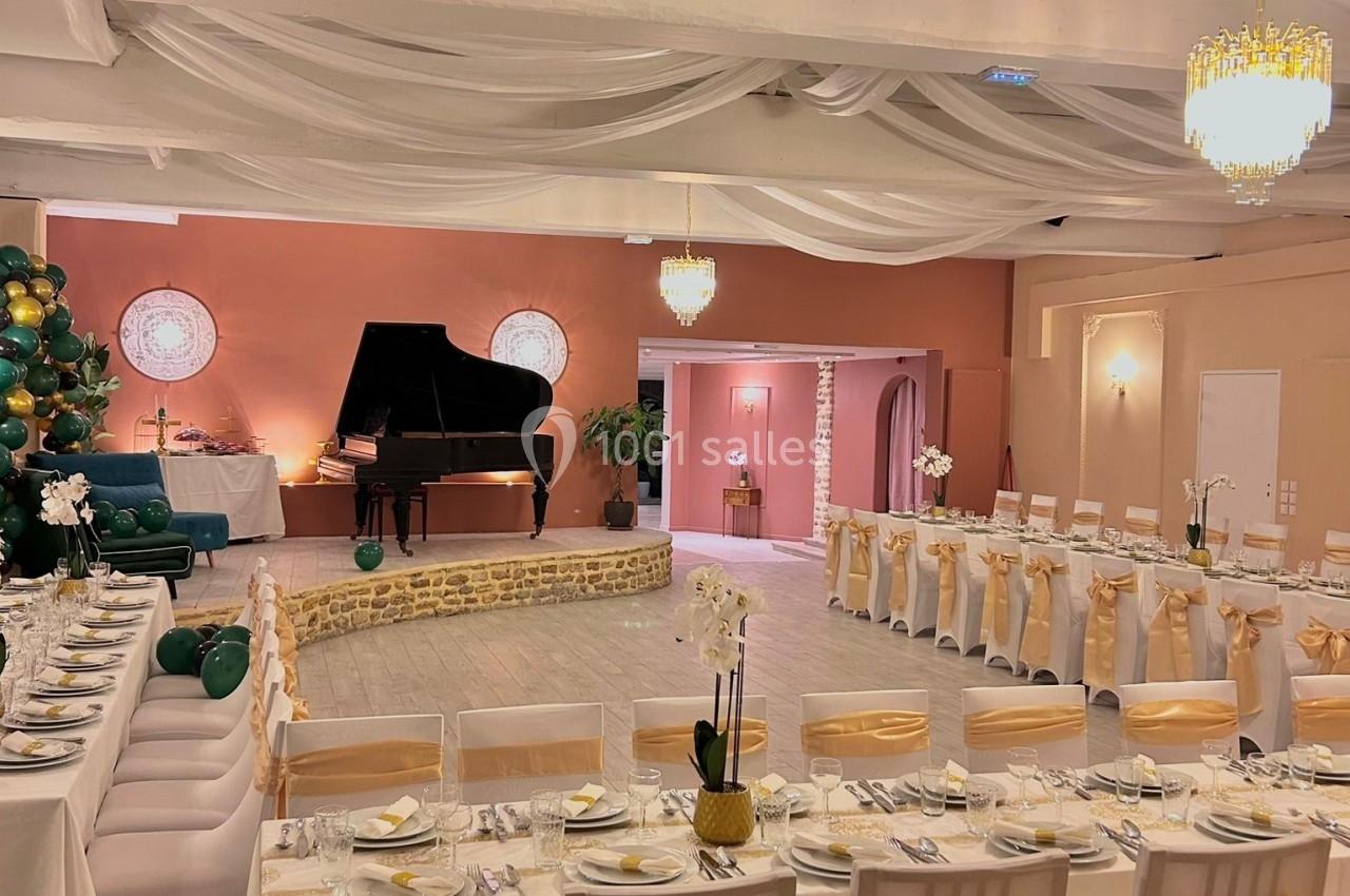 Salle de réception décorée avec des tables dressées, des chaises ornées de nœuds dorés et un piano à queue sur une estrade.