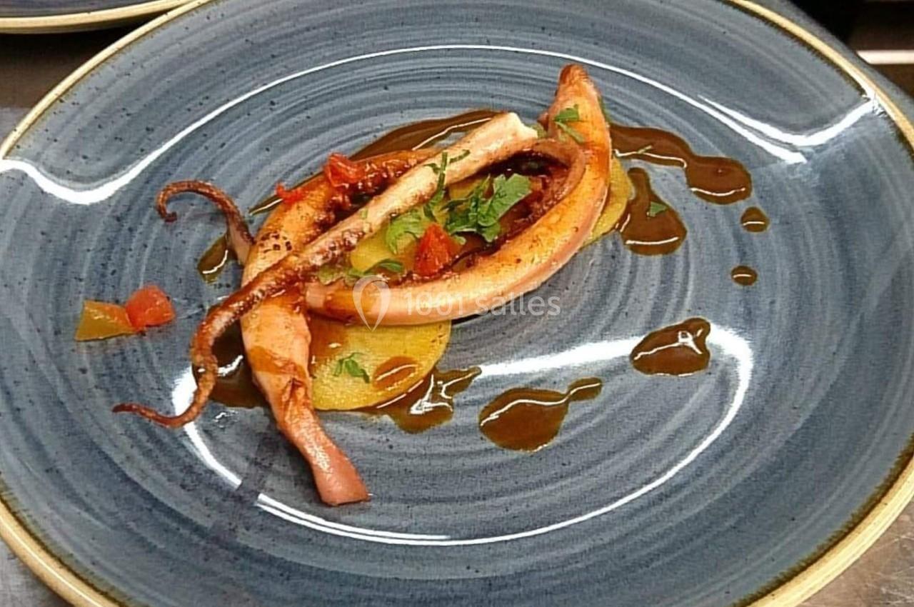 Assiette avec un calamar grillé, accompagné de légumes et d'une sauce disposée en filet sur une assiette bleue.