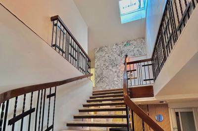 Salle lumineuse avec murs en pierre, mobilier moderne, lampes rouges suspendues et vue sur une entrée vitrée.