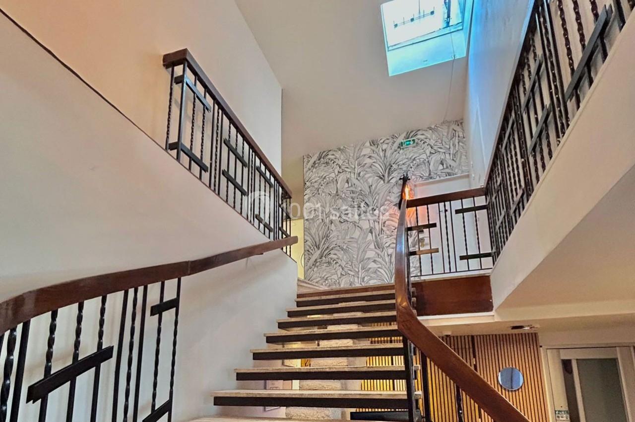 Escalier intérieur en bois et métal avec mur décoré de motifs végétaux et puits de lumière au plafond.