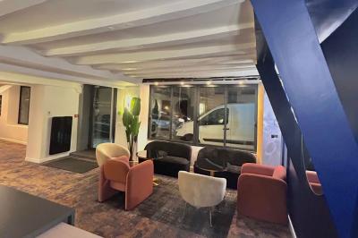 Salle lumineuse avec murs en pierre, mobilier moderne, lampes rouges suspendues et vue sur une entrée vitrée.