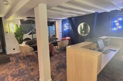 Salle lumineuse avec murs en pierre, mobilier moderne, lampes rouges suspendues et vue sur une entrée vitrée.