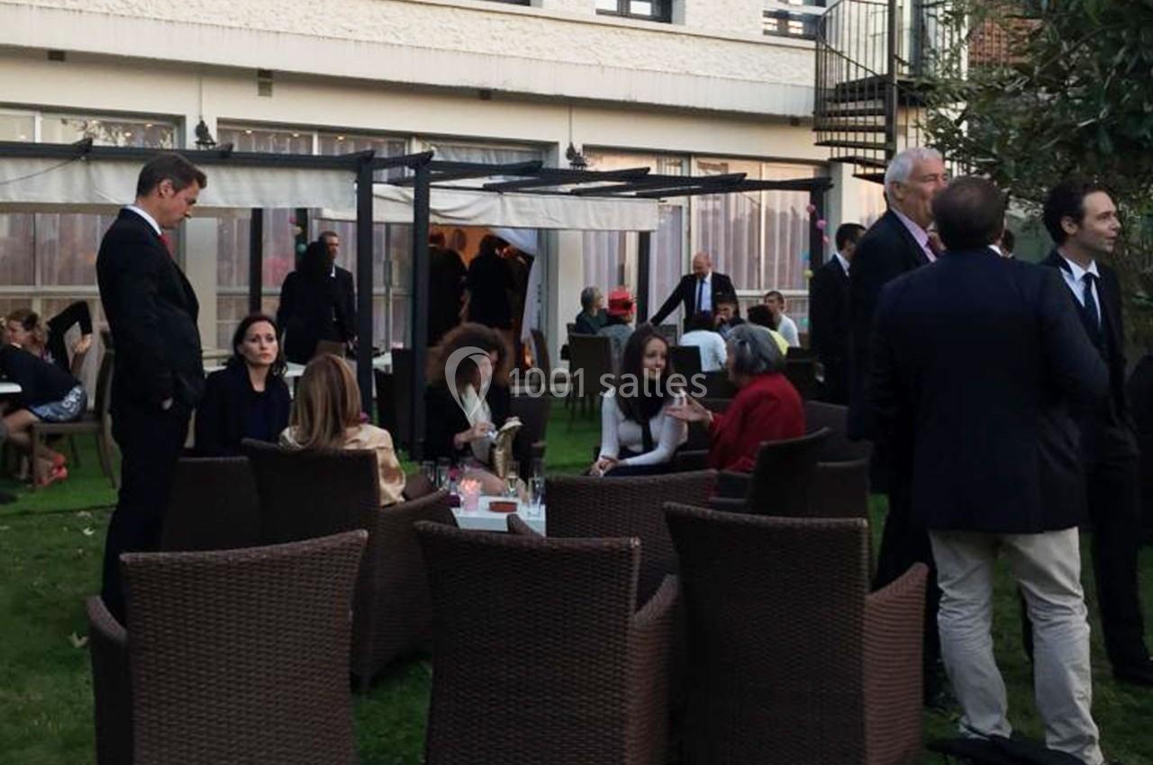 Personnes discutant en petits groupes dans un jardin, assises ou debout, entourées de mobilier d'extérieur.