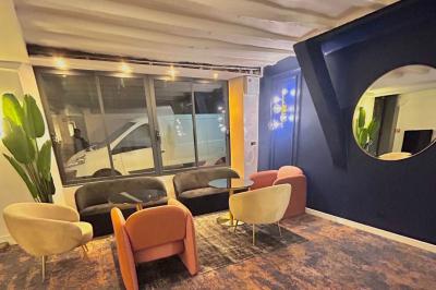 Salle lumineuse avec murs en pierre, mobilier moderne, lampes rouges suspendues et vue sur une entrée vitrée.