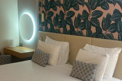 Salle lumineuse avec murs en pierre, mobilier moderne, lampes rouges suspendues et vue sur une entrée vitrée.