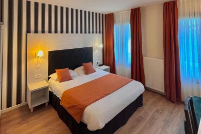 Salle lumineuse avec murs en pierre, mobilier moderne, lampes rouges suspendues et vue sur une entrée vitrée.