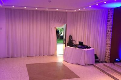 Salle lumineuse avec murs en pierre, mobilier moderne, lampes rouges suspendues et vue sur une entrée vitrée.