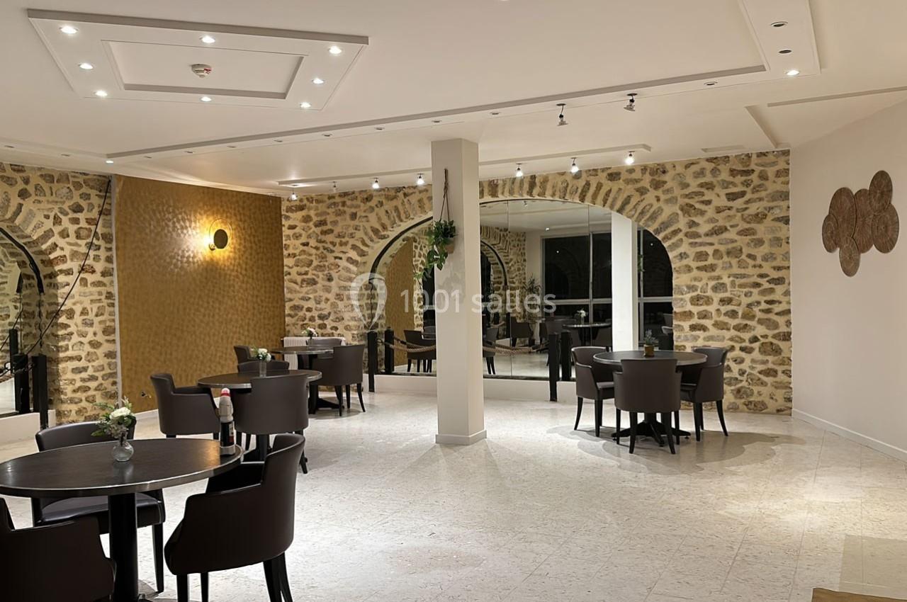 Salle de restaurant lumineuse avec murs en pierre, tables rondes espacées et décorations murales modernes.