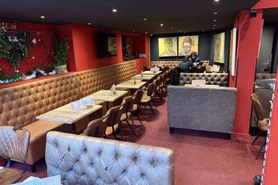 Vue d'un piano à queue dans un restaurant à la décoration chaleureuse avec murs rouges et tables alignées.