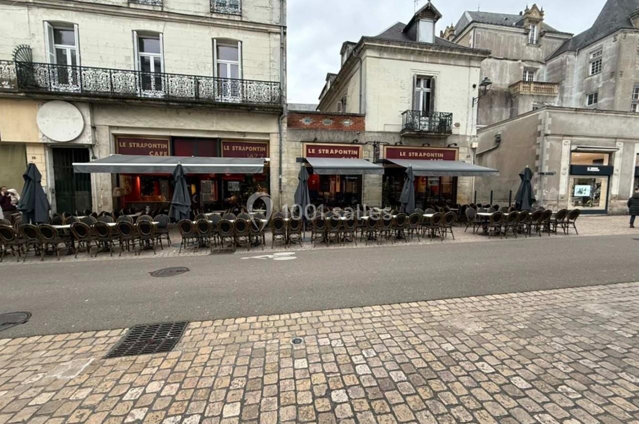 Façade d'un café avec terrasse vide, rangée de chaises et tables alignées, située dans une rue pavée.