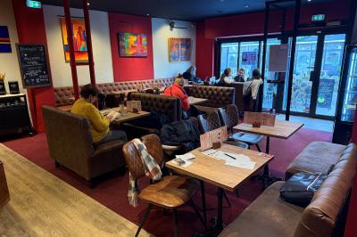 Vue d'un piano à queue dans un restaurant à la décoration chaleureuse avec murs rouges et tables alignées.