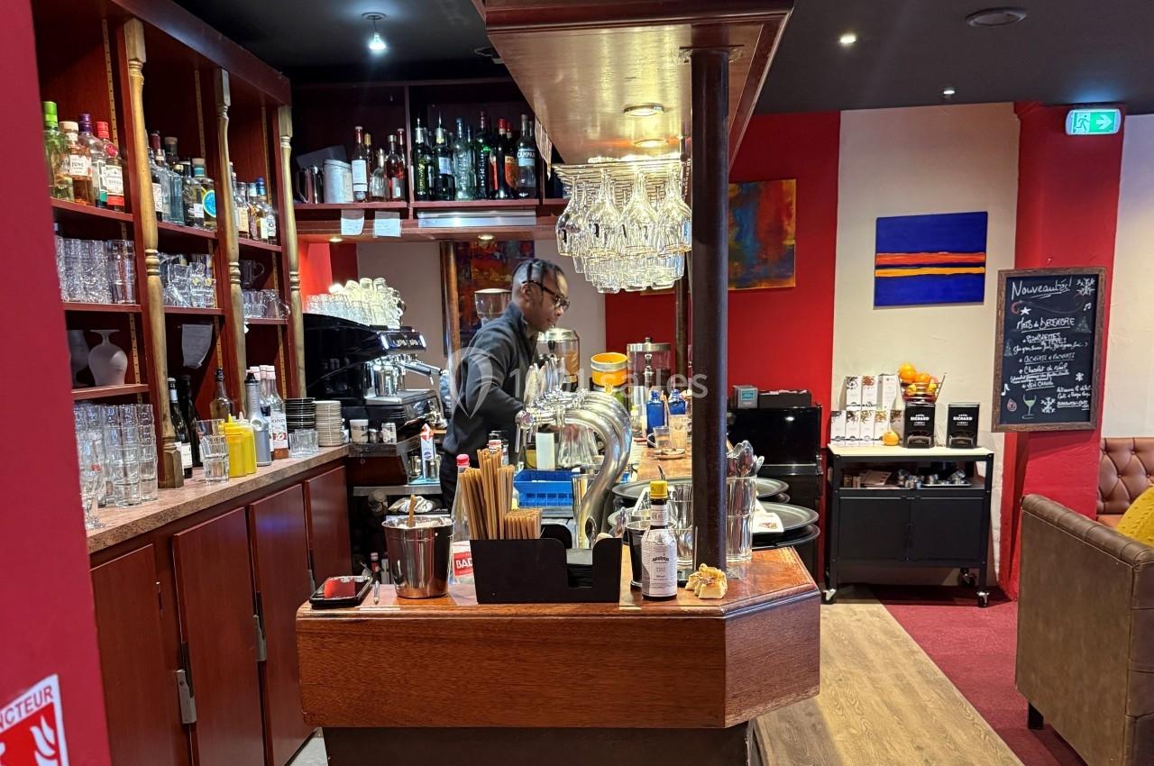 Un barman prépare des boissons derrière un comptoir en bois dans un bar à l'ambiance chaleureuse et colorée.