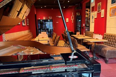 Vue d'un piano à queue dans un restaurant à la décoration chaleureuse avec murs rouges et tables alignées.