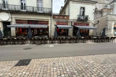 Terrasse vide d'un café avec des chaises alignées, devant une façade en pierre dans une rue pavée.