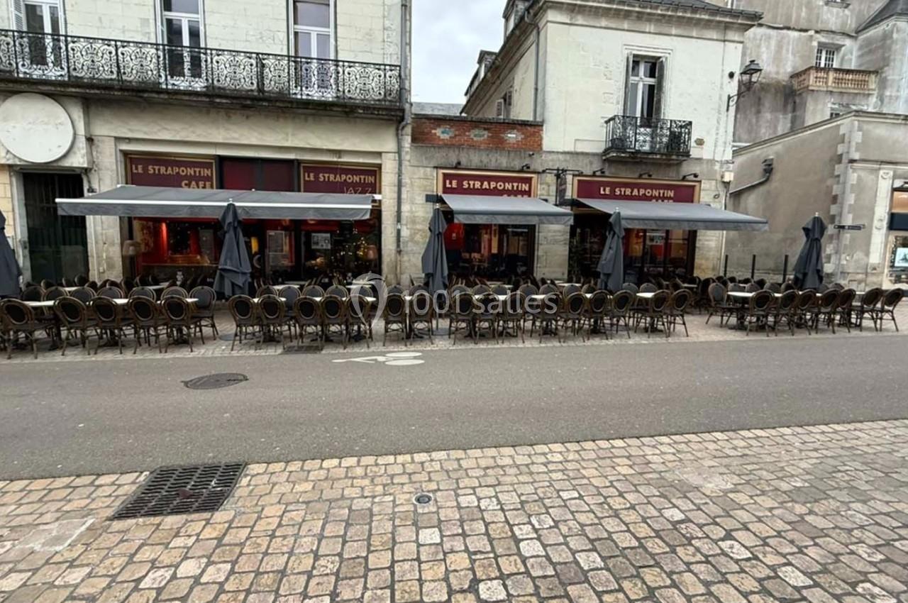 Terrasse vide d'un café avec des rangées de chaises et tables alignées devant une façade en pierre.