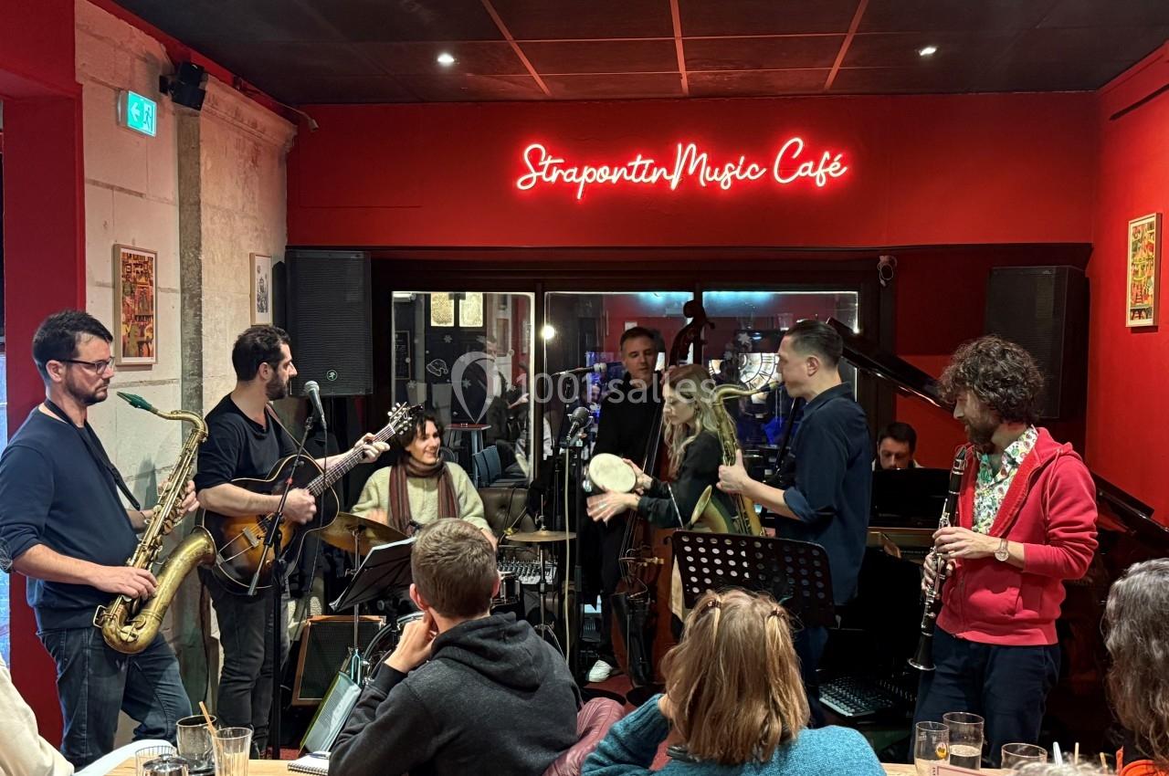 Groupe de musiciens jouant en live dans un café à l'ambiance chaleureuse, devant un public attentif.