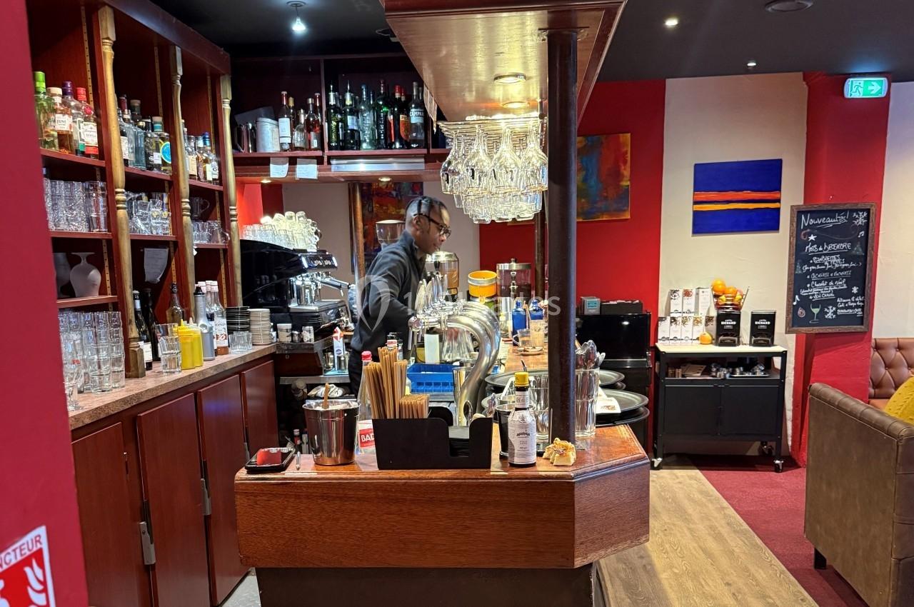 Un serveur prépare des boissons derrière un comptoir en bois dans un bar à l'ambiance chaleureuse et colorée.