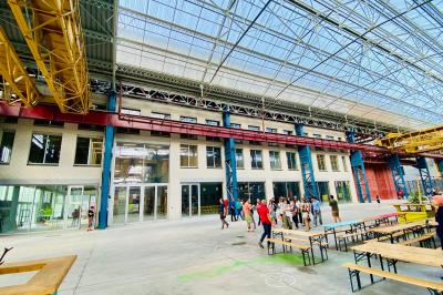 Salle de classe moderne avec tables en U, chaises en bois, sol en béton et éclairage suspendu.