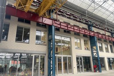 Salle de classe moderne avec tables en U, chaises en bois, sol en béton et éclairage suspendu.