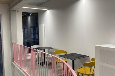 Salle de classe moderne avec tables en U, chaises en bois, sol en béton et éclairage suspendu.