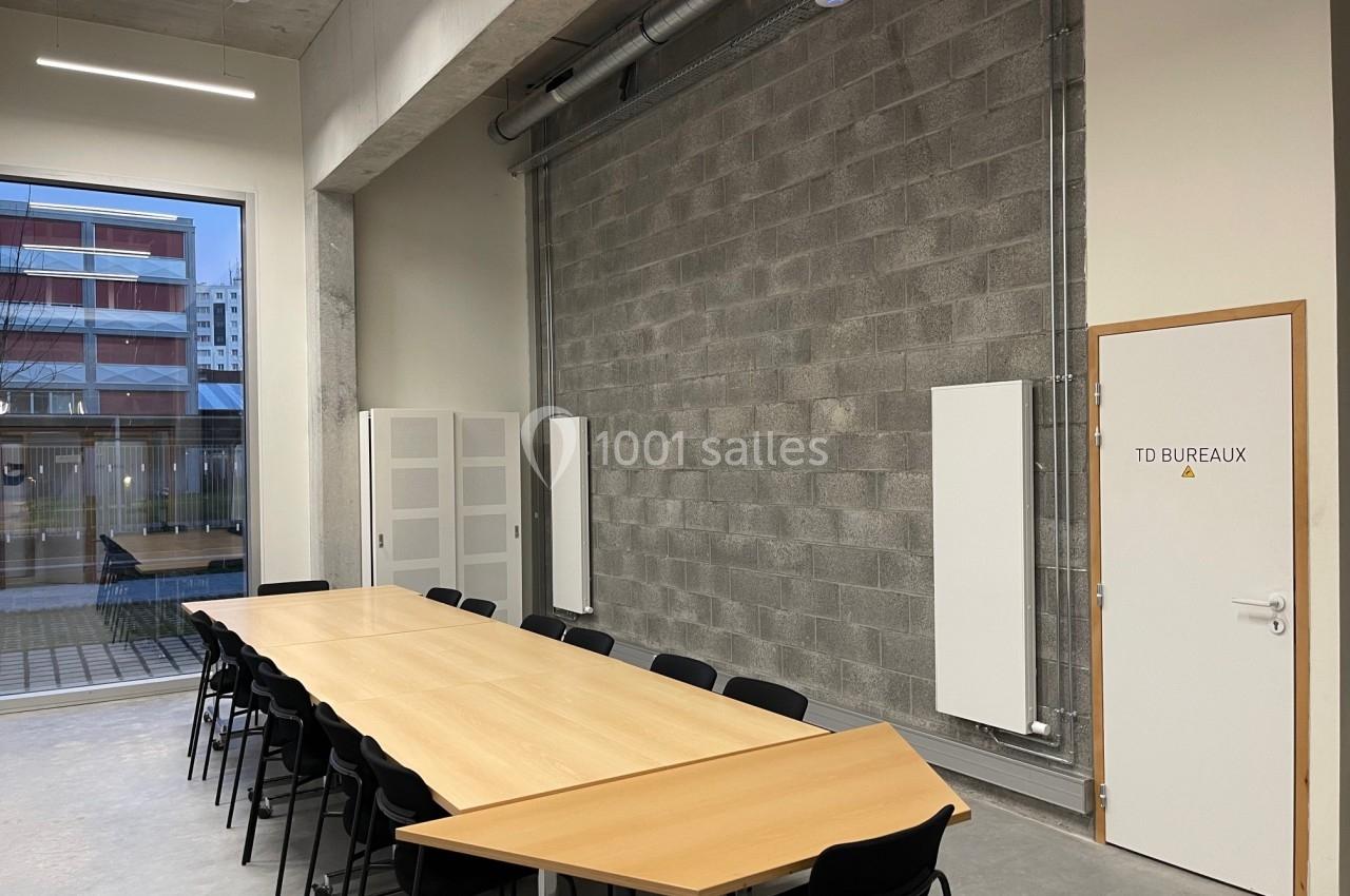 Salle de réunion avec une grande table en bois, chaises noires, murs en béton et une porte marquée ’TD Bureaux’.