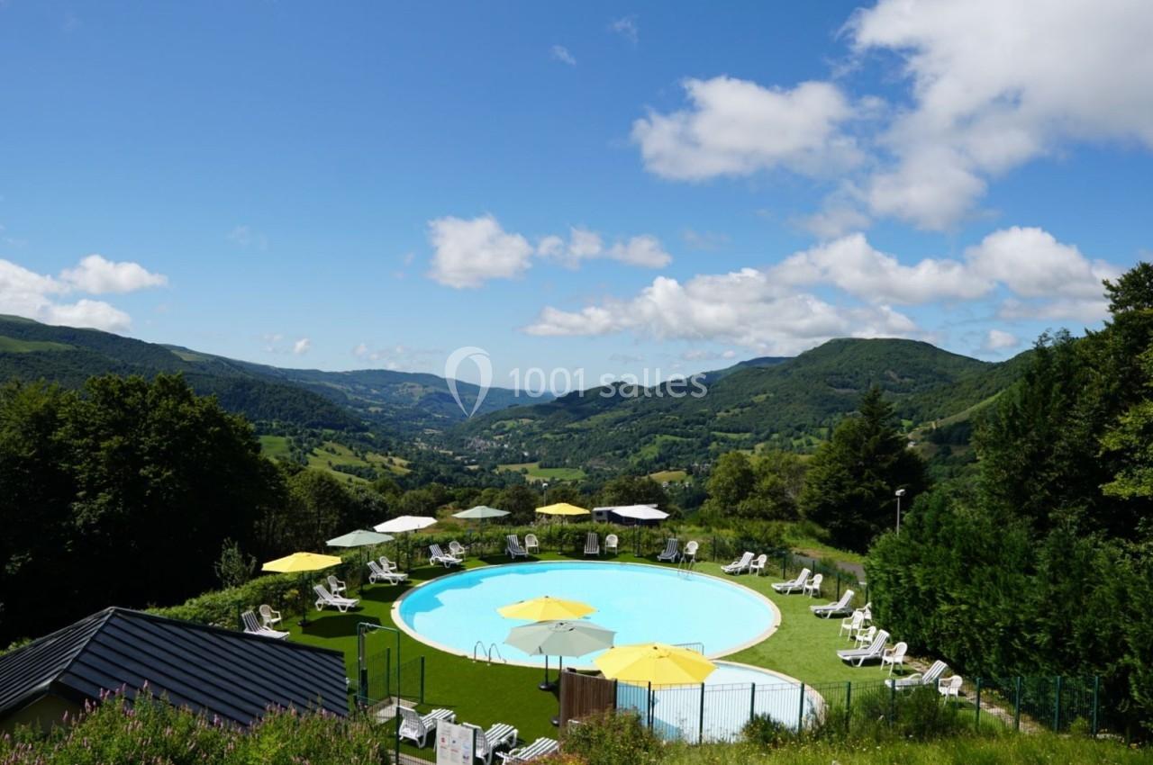 Piscine extérieure entourée de chaises longues et parasols jaunes, avec vue sur des collines verdoyantes sous un ciel bleu.