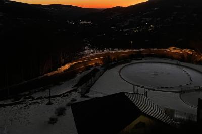 Salle de restaurant lumineuse avec poutres apparentes, grandes fenêtres, tables en bois et chaises hautes.