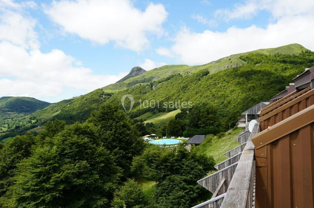 Vue sur une montagne verdoyante avec des arbres, une piscine en contrebas et une structure en bois au premier plan.