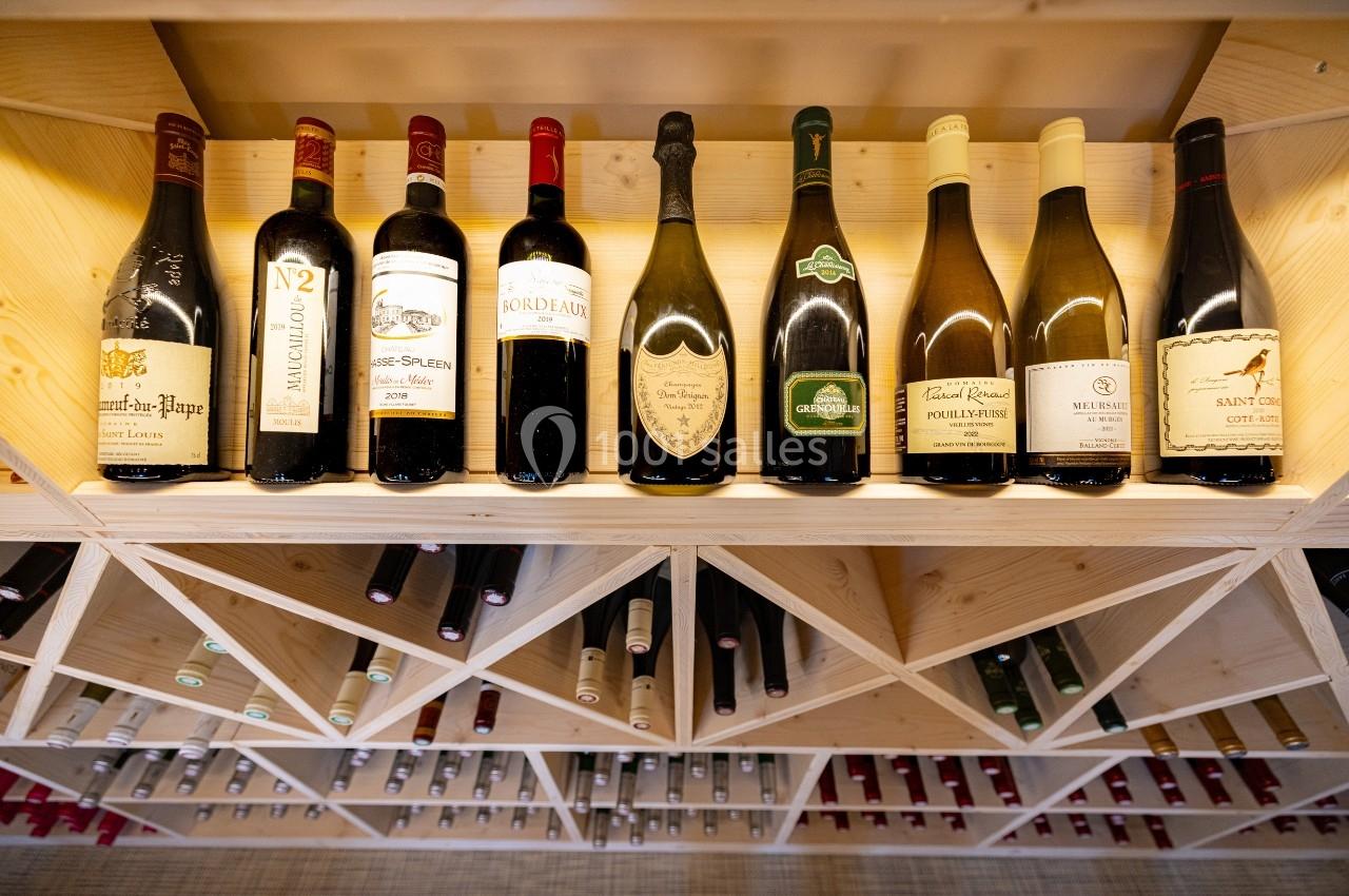 Bouteilles de vin rouge et blanc alignées sur une étagère en bois dans une cave à vin éclairée.