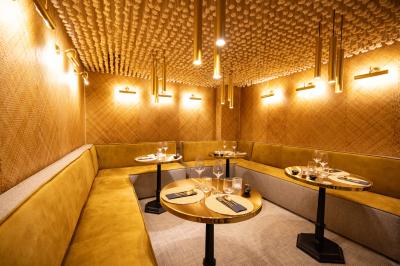 Salle de restaurant chaleureuse avec des tables dressées, une cave à vin visible et un serveur en action.