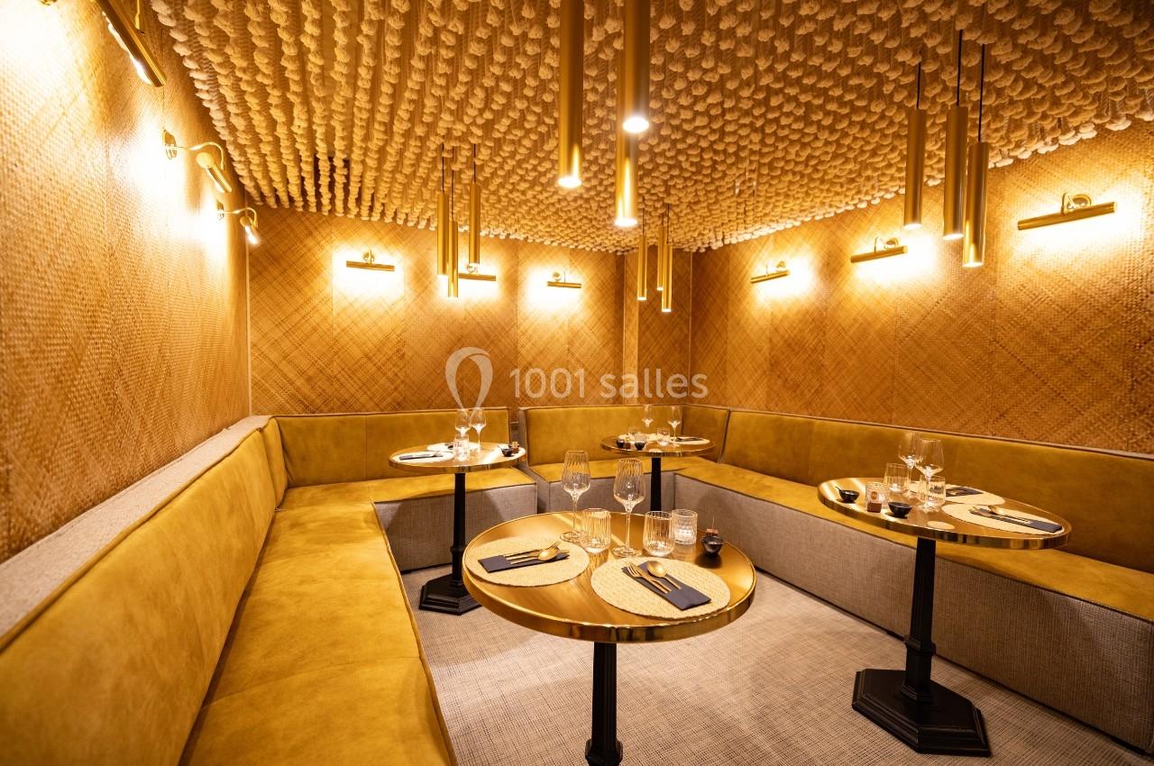 Salle de restaurant avec banquettes jaunes, tables rondes en bois, éclairage suspendu et plafond texturé.