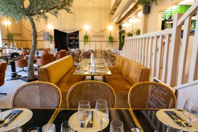 Salle de restaurant chaleureuse avec des tables dressées, une cave à vin visible et un serveur en action.