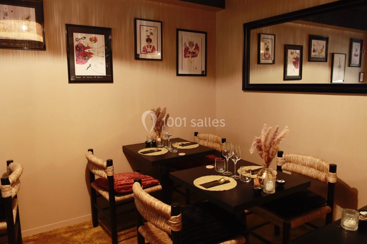 Salle de restaurant chaleureuse avec tables dressées, chaises en corde tressée et décorations murales encadrées.