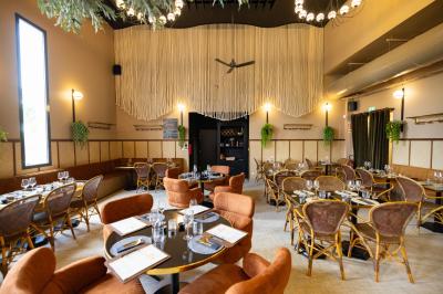 Salle de restaurant chaleureuse avec des tables dressées, une cave à vin visible et un serveur en action.