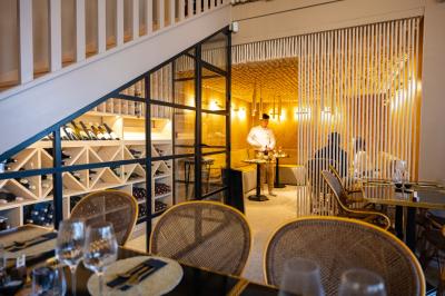 Salle de restaurant chaleureuse avec des tables dressées, une cave à vin visible et un serveur en action.