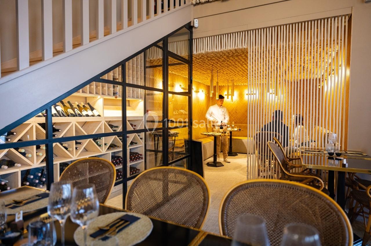 Salle de restaurant chaleureuse avec des tables dressées, une cave à vin visible et un serveur en action.