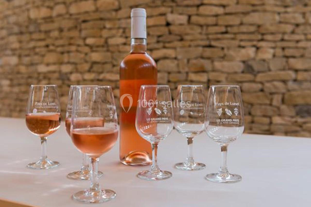 Bouteille de vin rosé et six verres partiellement remplis, posés sur une table devant un mur en pierre.