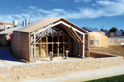Salle de réunion lumineuse avec tables en U, chaises en bois, tonneau décoratif et étagères murales garnies de bouteilles.